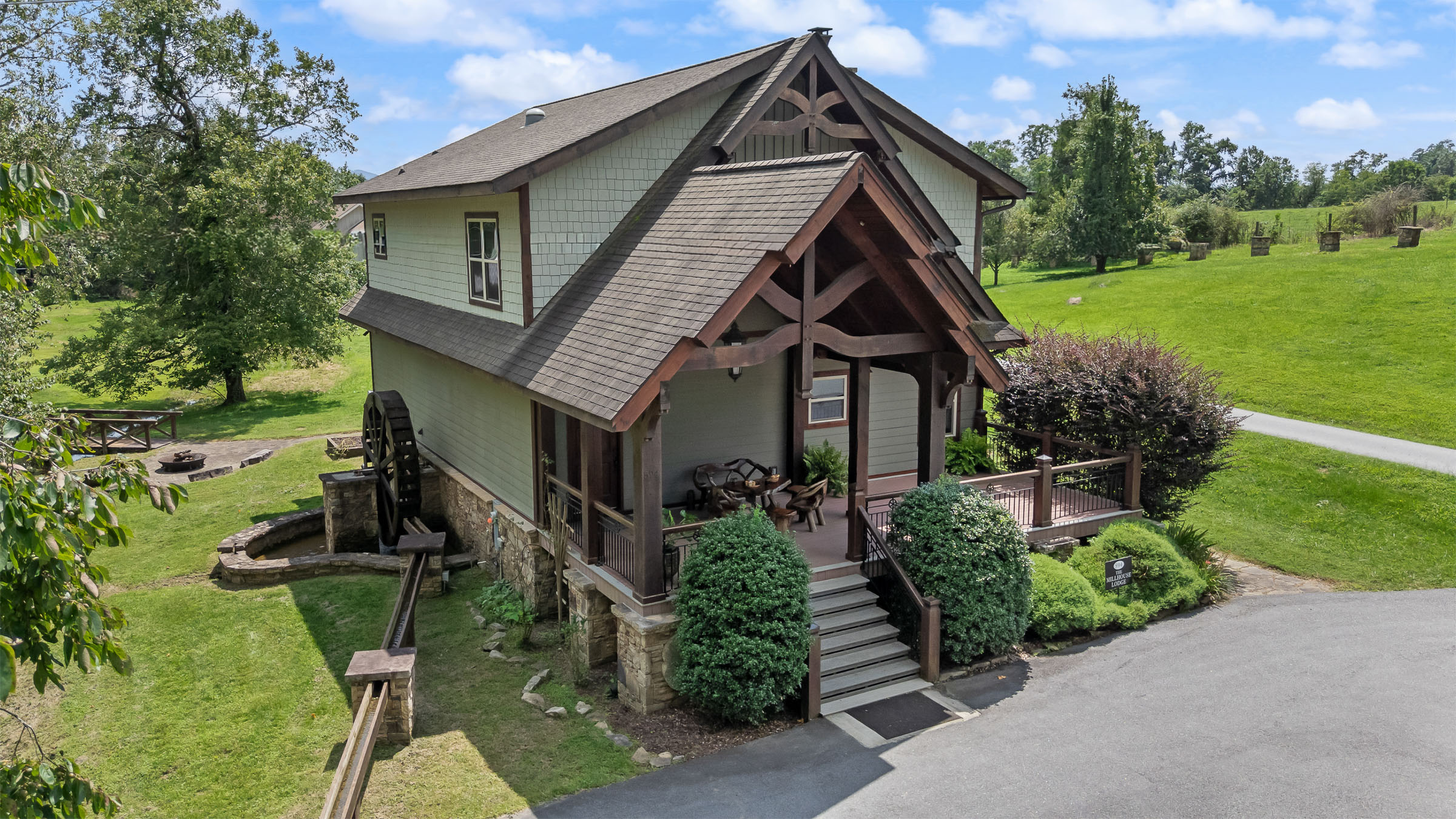 Aerial front exterior view of The Millhouse Lodge with timber entry, waterwheel, and green farm grounds