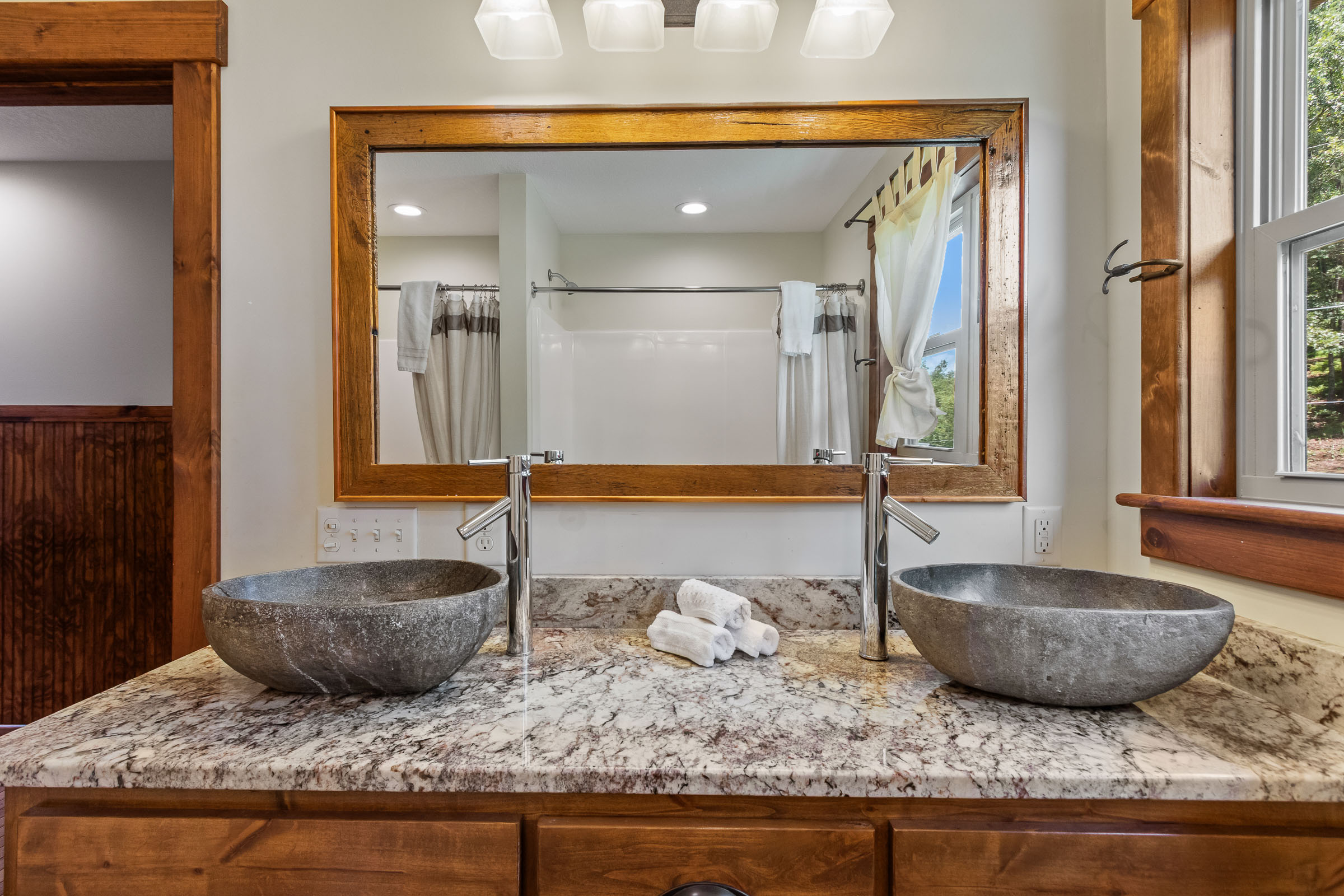 Bathroom at The Millhouse Lodge with double stone vessel sinks, granite counter, and wood-framed mirror