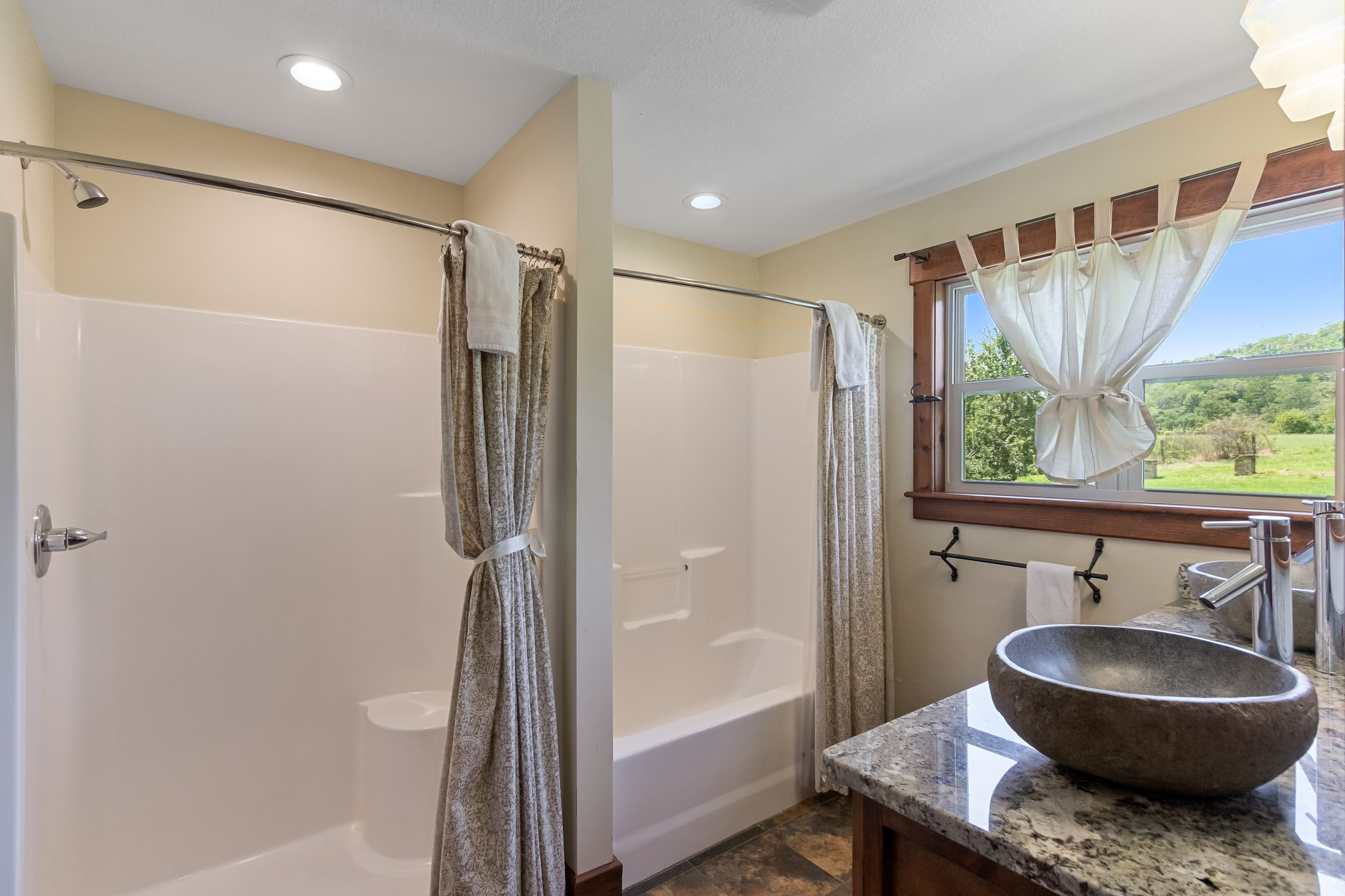 Bathroom at The Millhouse Lodge with shower, stone vessel sink, and window view of the farm