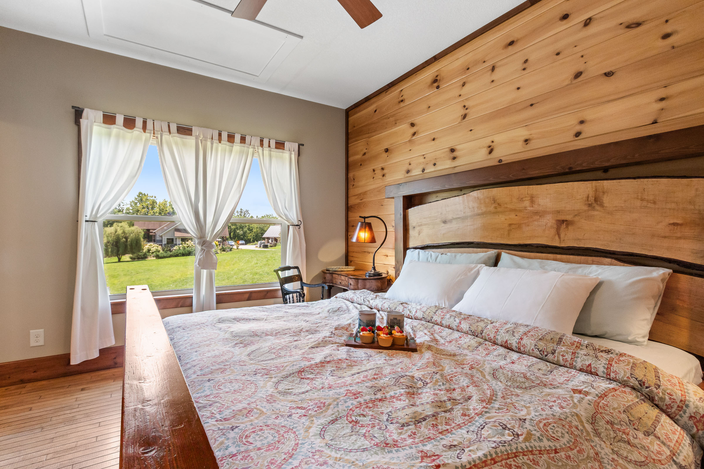 Bedroom at The Millhouse Lodge with wood headboard, white curtains, and farm view