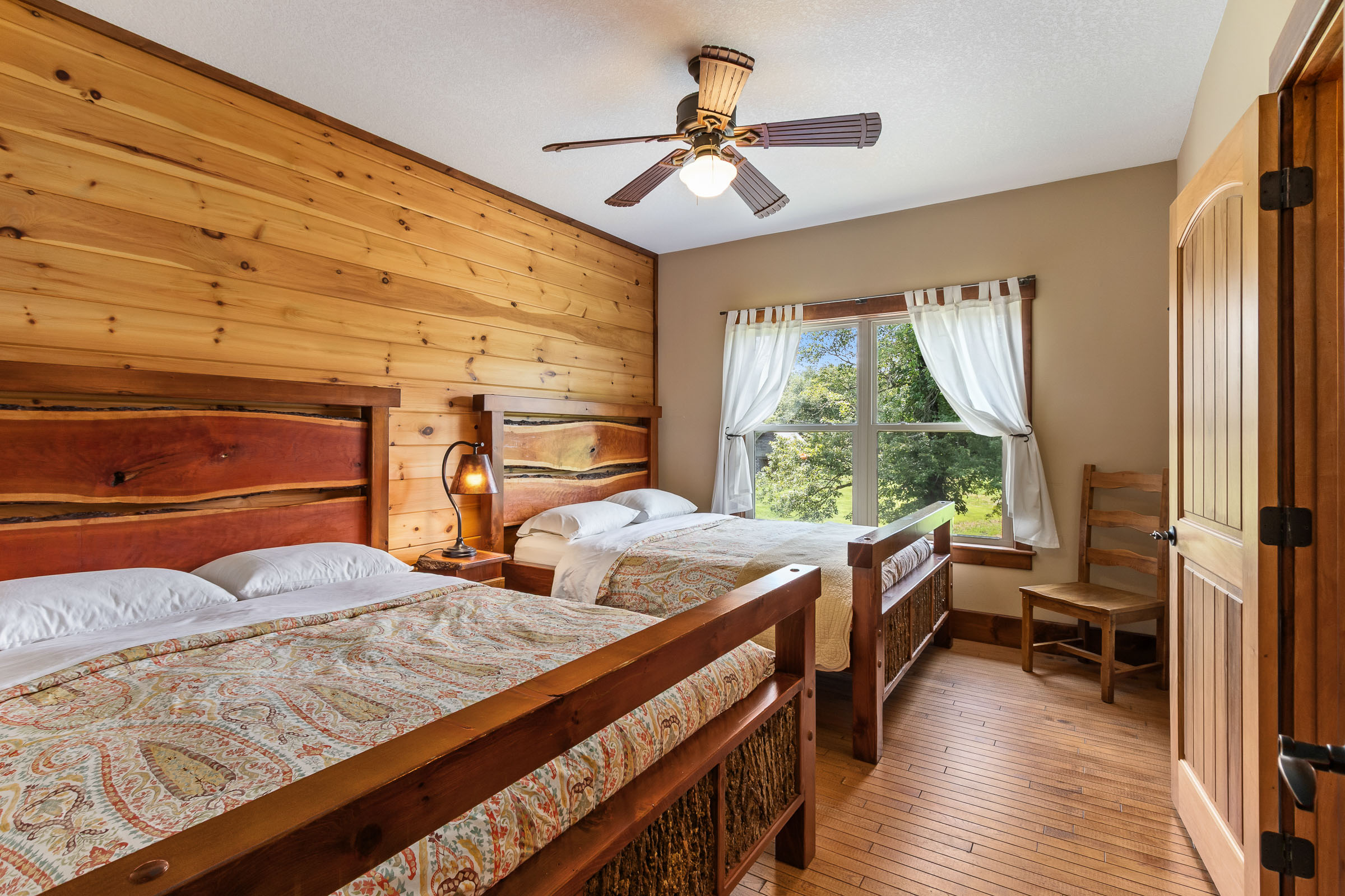 Bedroom at The Millhouse Lodge with two beds, wood accent wall, and window views