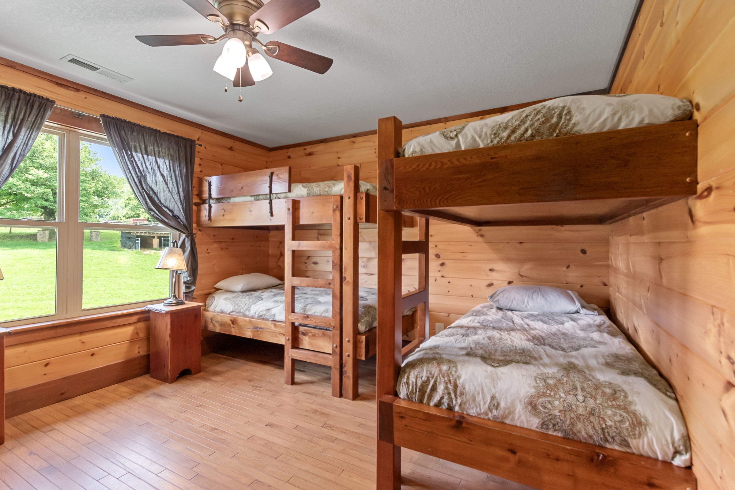 Bunk bedroom at The Millhouse Lodge with wood beds, bedside lamp, and farm window view