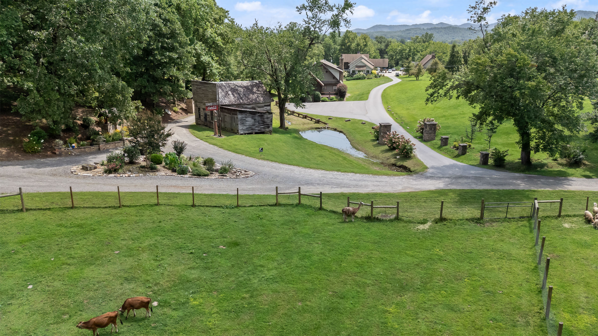 Overlook of The Millhouse Lodge and McGuire's Millrace Farm with lawns, driveway, and mountain trees