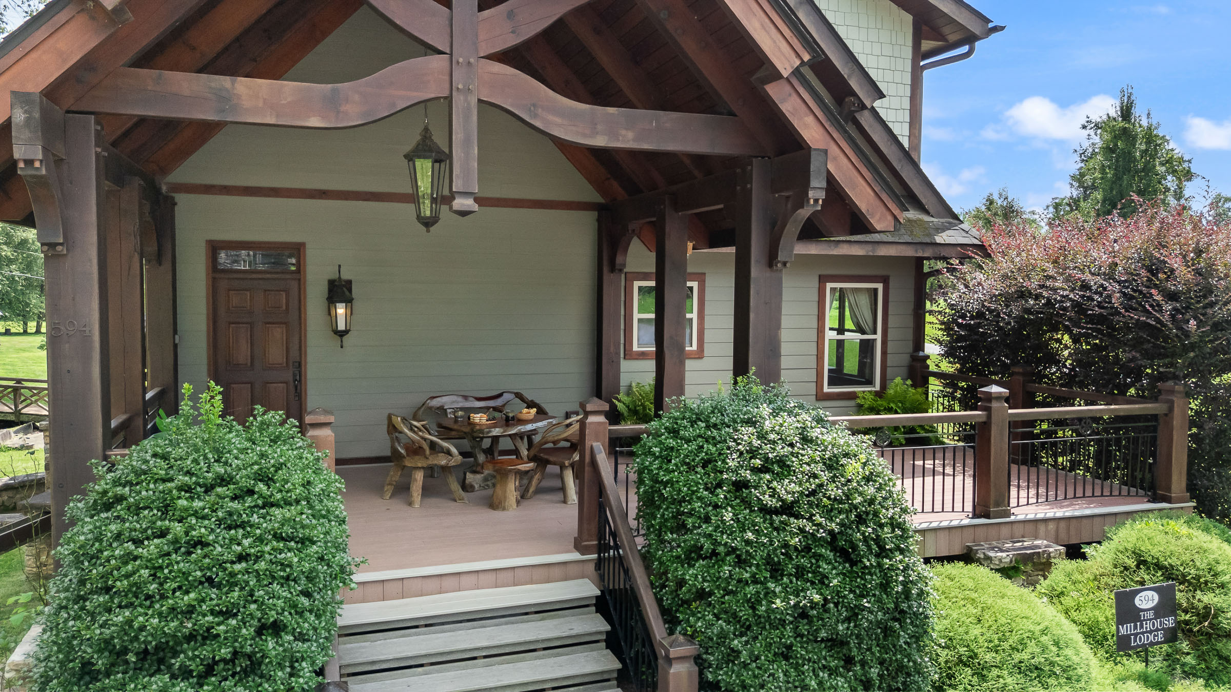 Front porch exterior of The Millhouse Lodge with timber beams, stairs, and lodge sign
