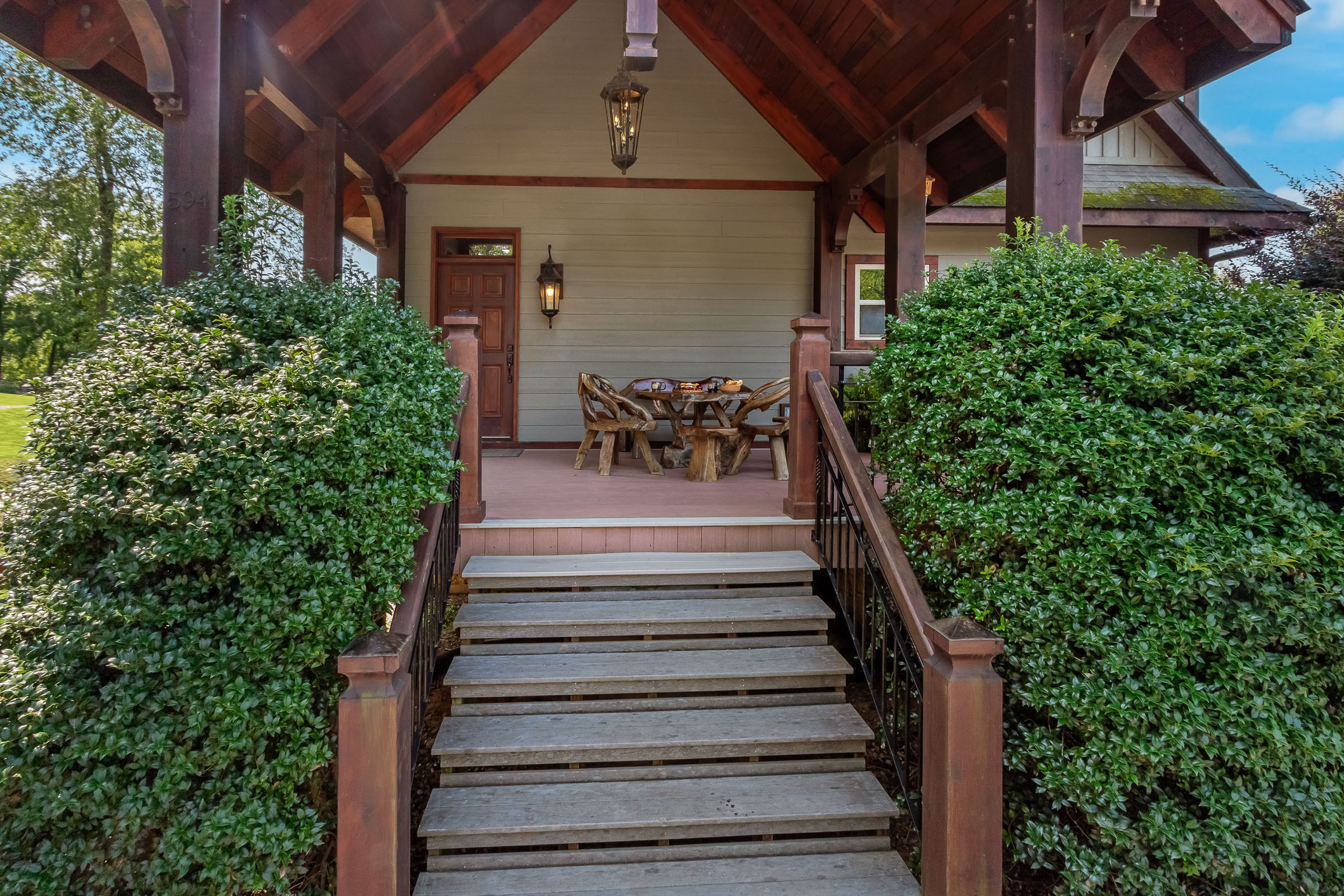 Front stairs and covered timber entry at The Millhouse Lodge framed by manicured shrubs